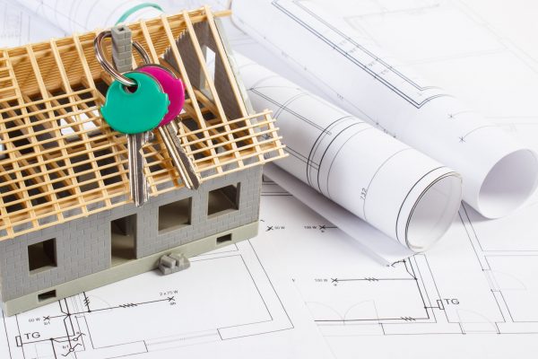 Small house under construction with home keys and electrical rolls of diagrams and drawings for project, concept of building home